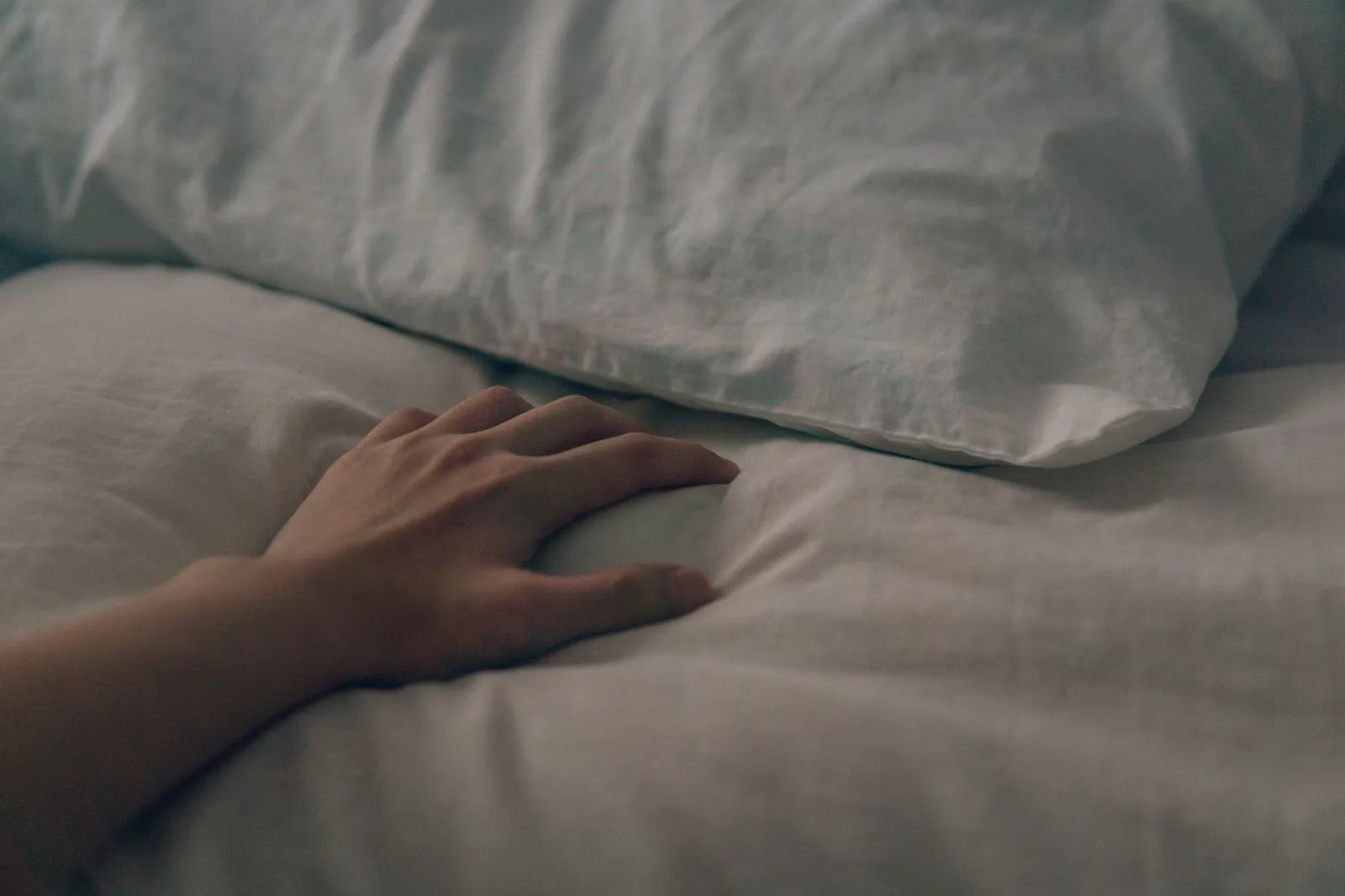 Main effleurant un tissu doux et texturé dans un intérieur clair, ambiance calme et chaleureuse.